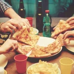 Pizza slices being shared by friends at a table.